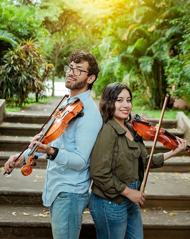 Portrait of two young violists back to back outdoors. Portrait of smiling male and female violinist back to back outdoors. Two young violinists back to back holding their violins