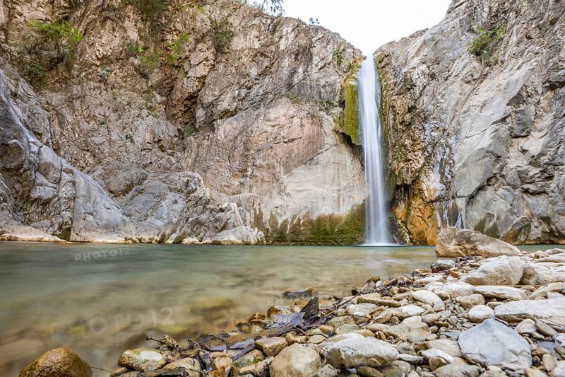 Scenic waterfall cascades into a tranquil pool surrounded by rugged rocks in Matacanes, Nuevo Leon, Mexico. The serene setting contrasts with the canyon's rough terrain