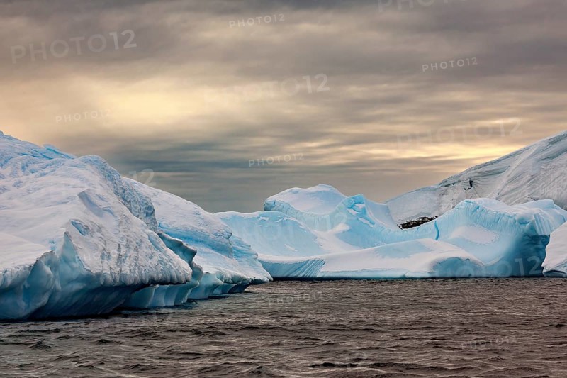 Huge, sharp icebergs stretch out under a cloudy sky as dusk falls, icebergs in the landscape of the Southern Ocean in Antarctica