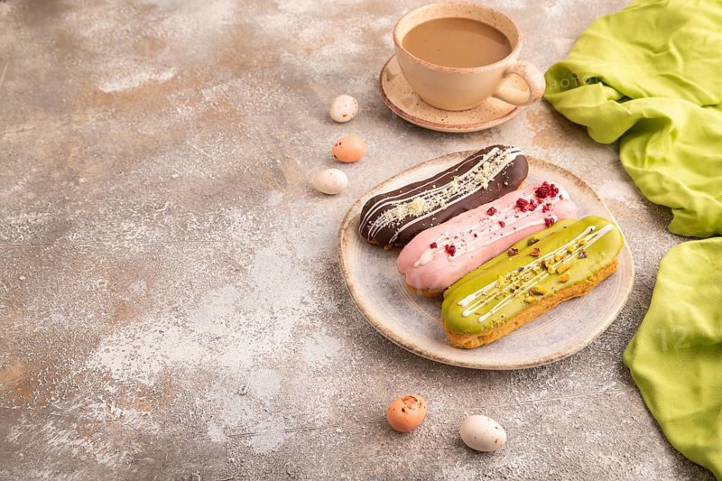 Glazed Eclairs on brown concrete background and green linen textile, cup of coffee, side view, copy space