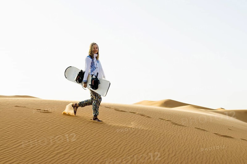 Young woman with snowboard in the sand dunes, near Merzouga, Meknès-Tafilalet region, Erg Chebbi, northern Sahara, Morocco