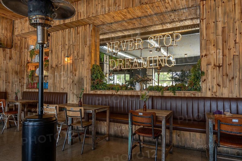 Warm, rustic cafe interior featuring wooden walls, vintage furniture, green plants, and a large mirror with a glowing neon sign that reads Never Stop Dreaming, creating an inspiring atmosphere