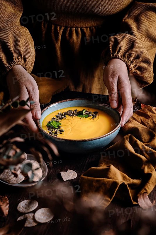 A warm autumn soup served in a ceramic bowl, garnished with seeds and herbs. The rich texture and autumnal colors create a cozy atmosphere, captured in dim lighting