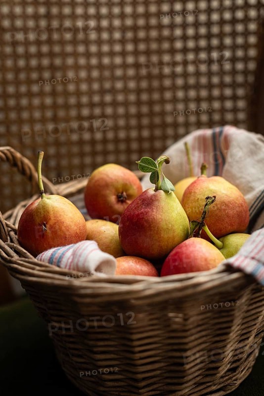 A charming wicker basket filled with ripe pears, resting on a striped textile. The warm tones and soft texture create a cozy, rustic ambiance perfect for country themed decor