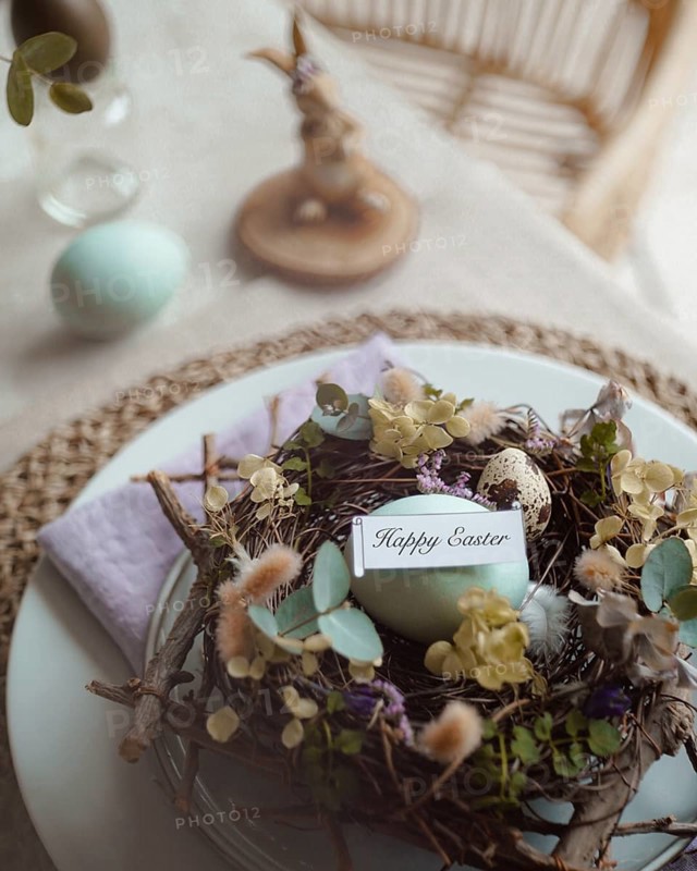 Top view of an elegantly arranged Easter table setting featuring naturally dyed eggs nestled in a decorative nest with spring flowers and a tag reading Happy Easter