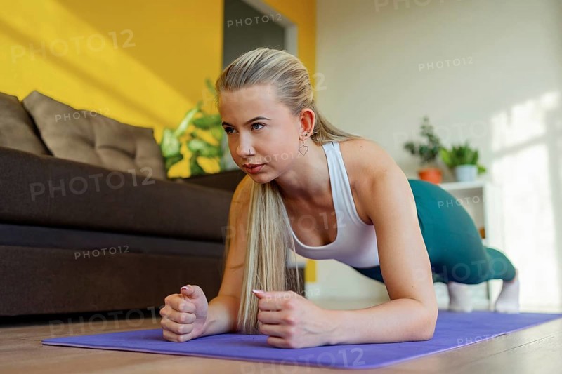 A woman performing a plank exercise on a yoga mat in her living room. Focused on core strength and fitness, surrounded by a comfortable and bright home setting