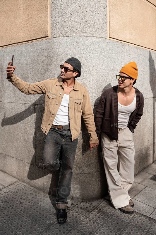 A Colombian couple taking a selfie, hand in hand. They lean against a city wall, embodying modern fashion and companionship. One takes a selfie, capturing the moment