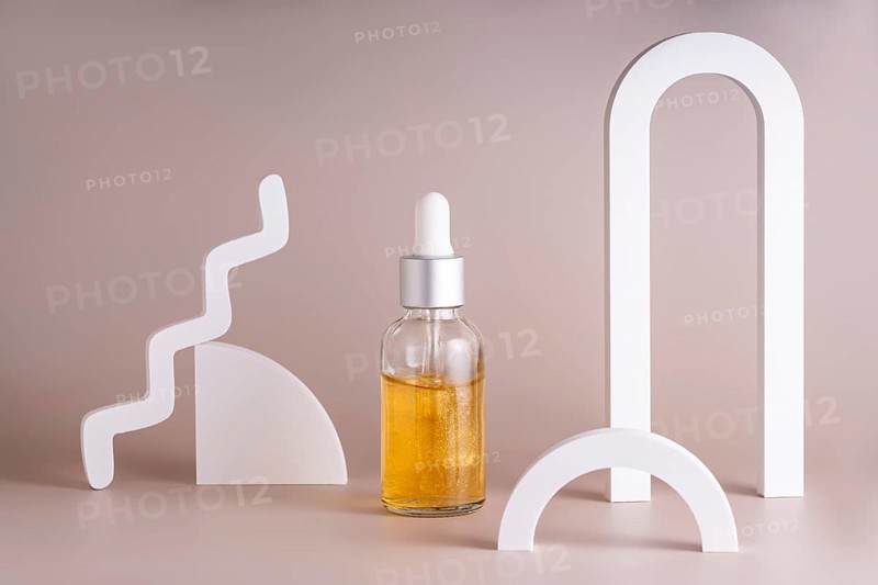 A modern cosmetic serum bottle with a silver dropper surrounded by minimalist geometric shapes on a soft beige background creates a stylish and elegant composition