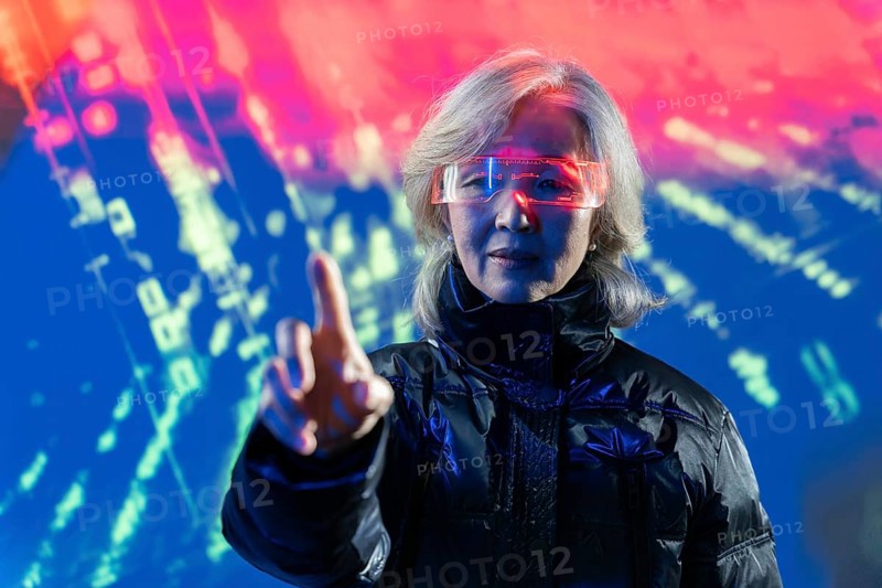 An elderly Asian woman in futuristic glasses interacts with digital elements in the metaverse, highlighting generational diversity in technology and virtual environments