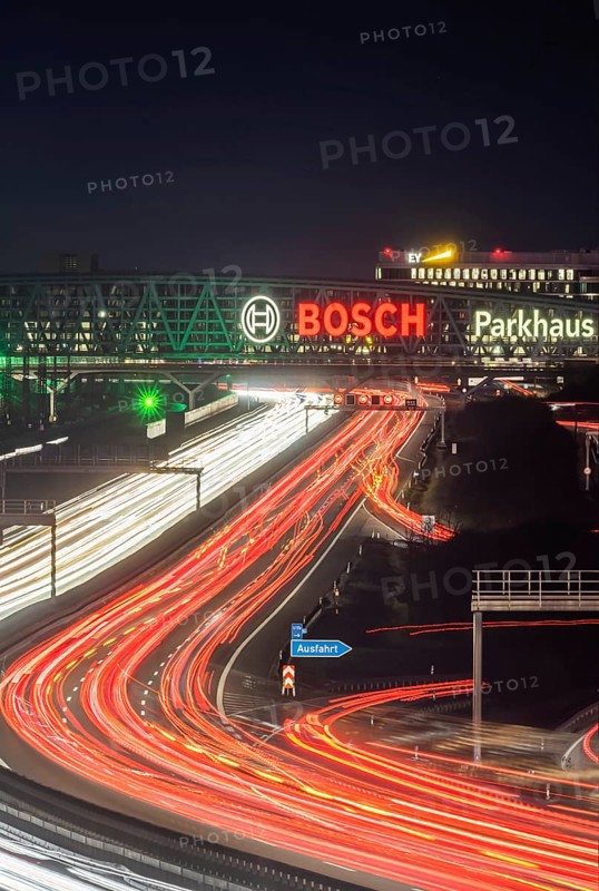 A8 motorway at Stuttgart Airport in the evening. Heavy traffic, lanes of light. Modern architecture of Messe Stuttgart with multi-storey car park above the motorway lanes. Logo of the Bosch company. Stuttgart, Baden-Württemberg, Germany