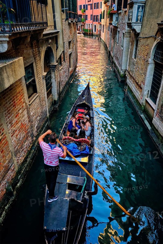 VENICE, ITALY, JUNE 27, 2018: Narrow canal between colorful old houses with gondola boat with tourists and gonolier in Venice, Italy