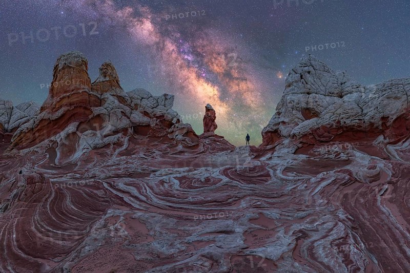 A lone man stands under the Milky Way, gazing at the stars over the unique geological formations of White Pocket, Arizona, USA, showcasing a breathtaking nightscape