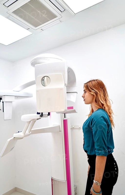 A young woman stands in a dental clinic, preparing for a panoramic dental X-ray. The advanced imaging machine ensures accurate diagnostics and effective dental care