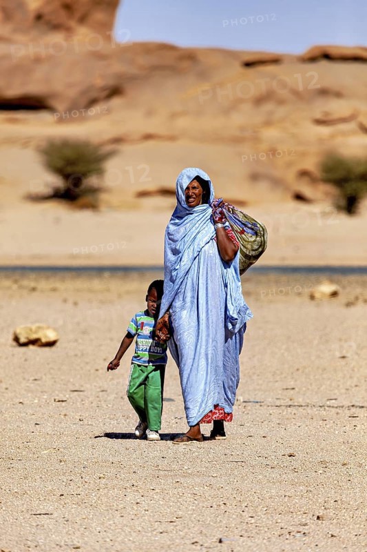 Mother and child in traditional dress walk together through a barren, sandy desert, woman in the Sahara in Algeria