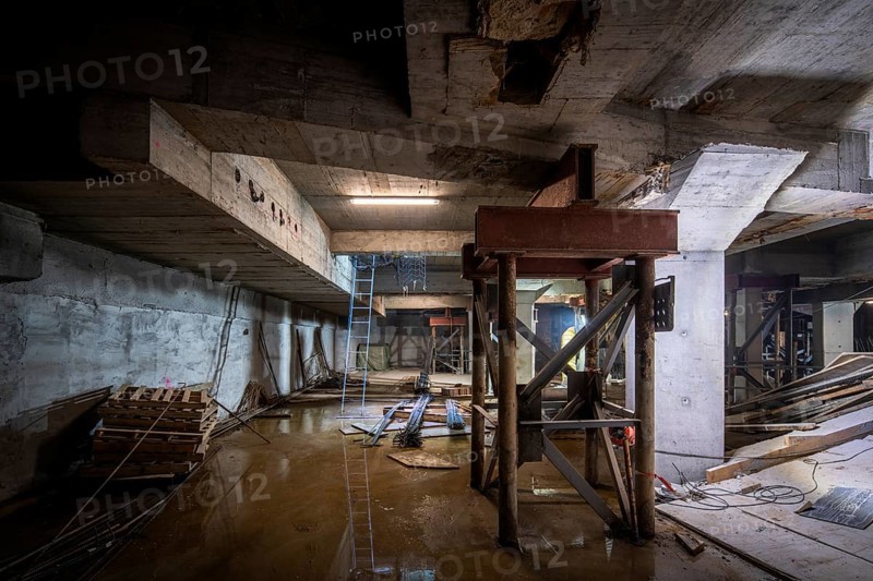 A dimly lit basement under construction, with structural beams and tools scattered about. The work shows progress and potential, highlighting the intricate details of the building's development