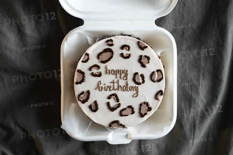 Top view of a stylish bento birthday cake with happy birthday message, neatly presented in a white takeout box against a textured gray background