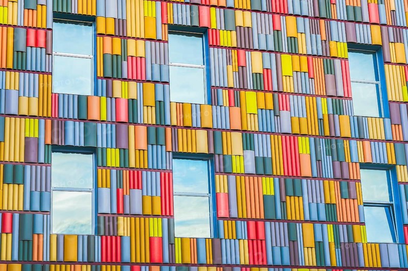 A detailed view of a building facade covered in a multitude of brightly colored panels arranged in a geometric pattern, highlighting modern architectural design elements
