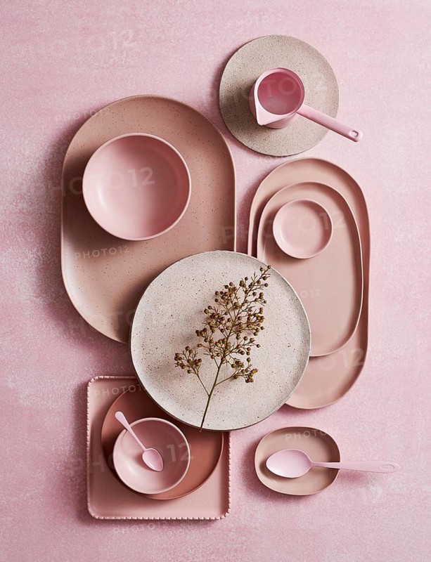 Top view of an artistic arrangement of ceramic crockery, featuring various shades of pink and rustic textures. A delicate dried flower complements the smooth and matte finishes