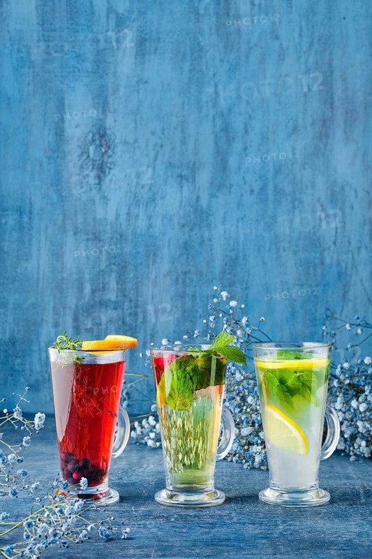 Three glasses with hot fruit and herbal tea on blue background