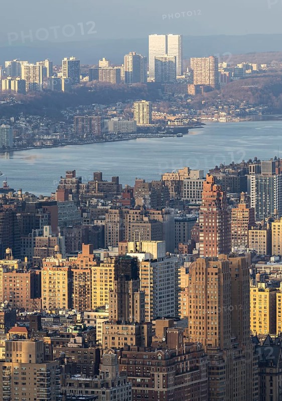Top view of New York City during sunset, showcasing a panoramic view of buildings bathed in golden light with the Hudson River and New Jersey in the background