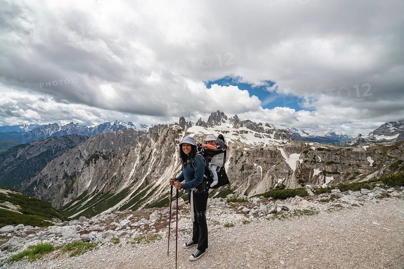 A smiling mother with her baby in a carrier hikes through the breathtaking snow-capped peaks of Tre Cime di Lavaredo in the Dolomites, Italy. A moment of adventure, bonding, and natureâ€™s beauty