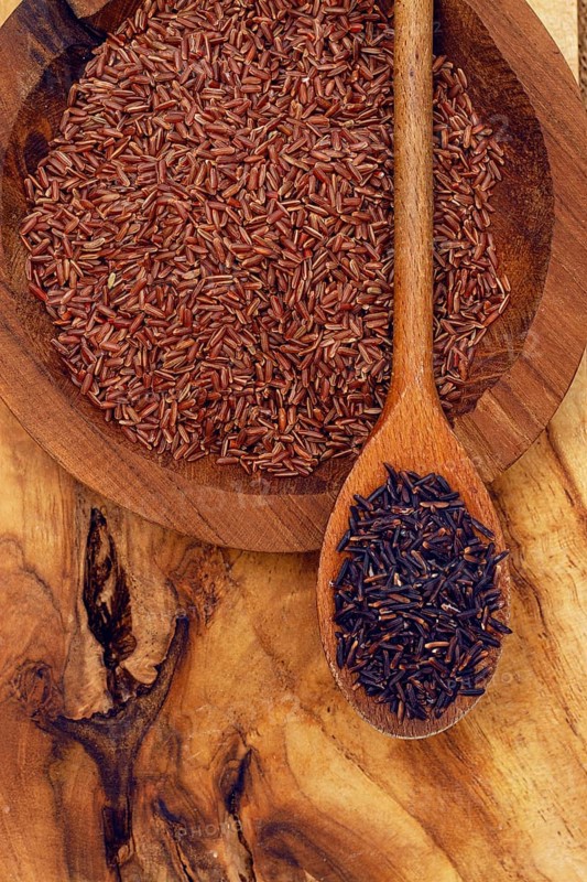 Red and black rice, in a wooden bowl and spoon on a wooden surface in rustic style, top view