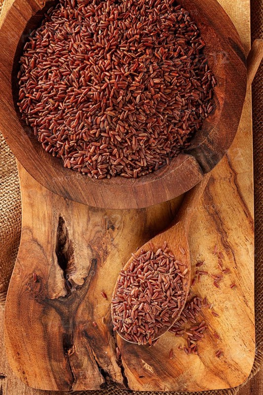 Natural, red rice, in a wooden bowl and spoon on a wooden surface in rustic style, top view
