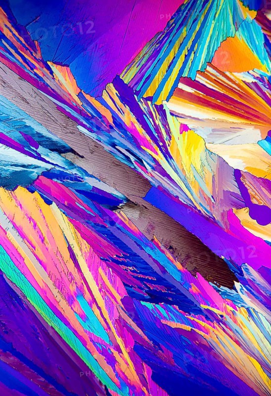 This striking image depicts the colorful patterns of Adipic acid crystals under a microscope, showcasing a vivid array of blues, purples, yellows, and pinks