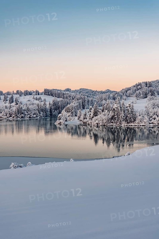 Dawn and sunrise at the wintry Forggensee in a snow-covered winter landscape in the foothills of the Alps in the Allgäu in Bavaria, Germany