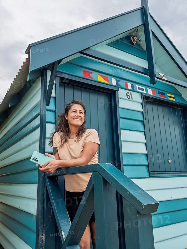 A woman standing on the steps of a colorful Brighton Bathing Box in Melbourne, Australia. The iconic beach huts are known for their vibrant stripes and classic architecture