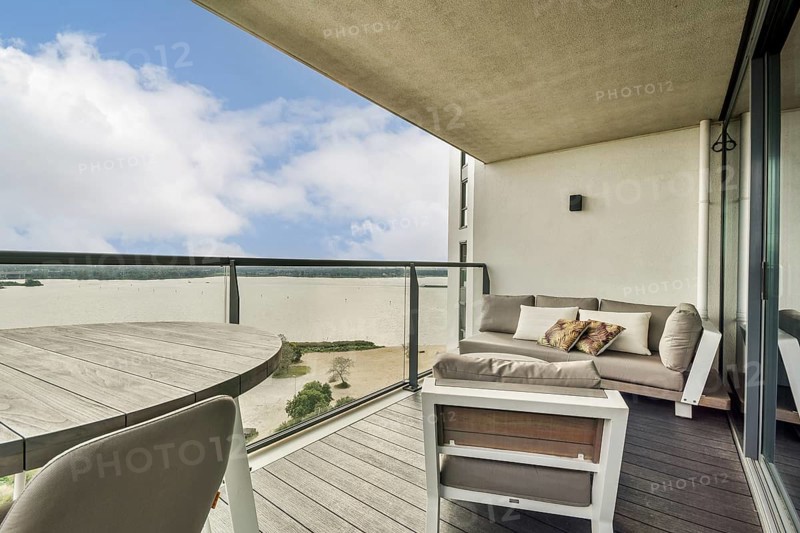 A stylish balcony featuring a cozy seating area overlooking a serene water view and bright sky, ideal for relaxation and leisure