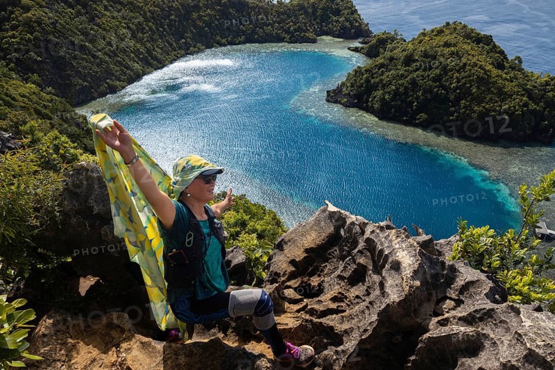 A traveler embraces nature on a cliff overlooking the stunning blue waters and lush greenery of Raja Ampat Archipelago, Indonesia, ideal for ecotourism