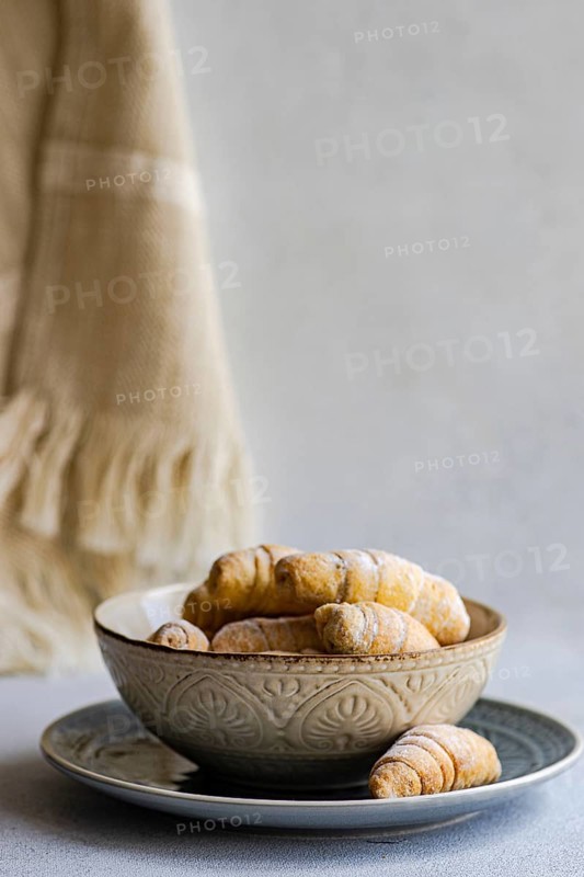 A decorative bowl filled with freshly baked homemade pastries, placed on a plate. The pastries are lightly dusted with sugar, creating an inviting and warm presentation