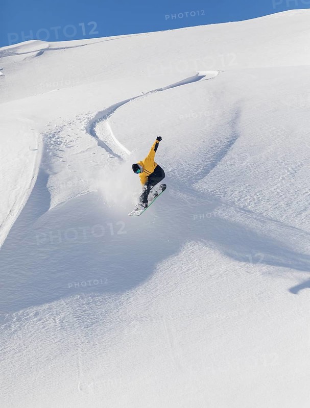 A snowboarder in a yellow jacket executes a jump on a snowy mountain slope. The clear blue sky and untouched snow add to the thrill and beauty of this winter sport