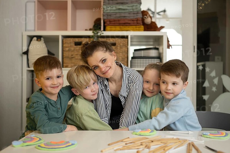 A teacher and four children smiling in a colorful classroom setting, surrounded by crafts and educational materials, representing joyful learning and creativity in education