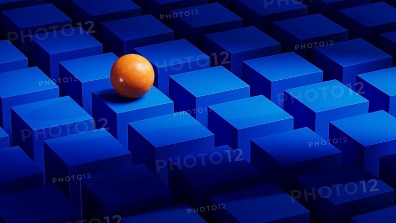 An orange sphere balances on a series of blue geometric forms. The abstract arrangement creates a visually striking composition in three dimensions