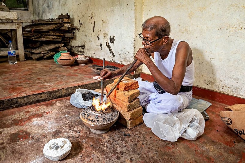 A man blows into a coal-fired pool with a concentrated face, a man burns sapphires in a small stove in the town of Ratnapura in Sri Lanka