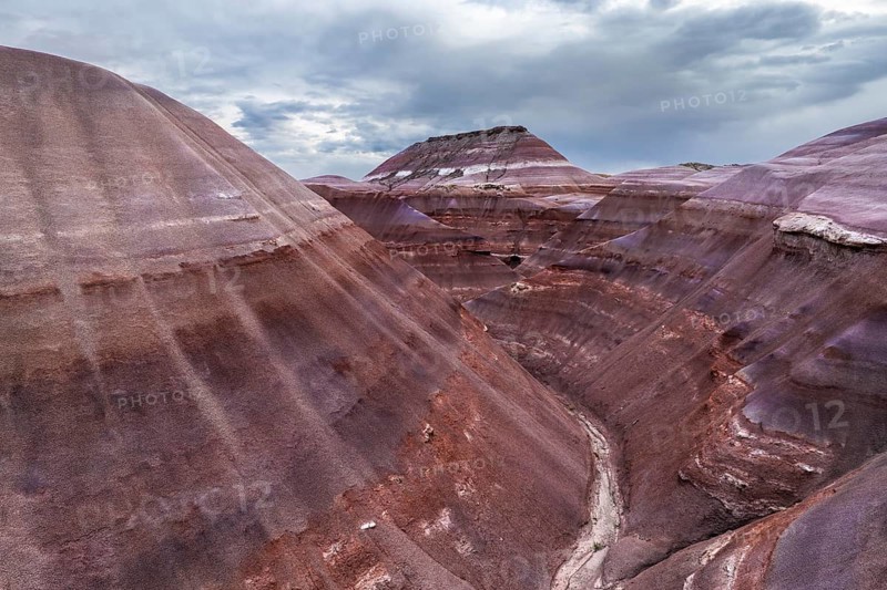A stunning drone photograph capturing the layered geological formations unique to Hanksville, Utah, showcasing a spectrum of earthen colors under a moody sky
