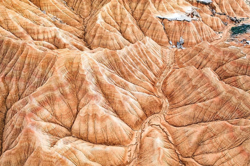 Aerial shot captures a striking desert landscape with rugged, eroded hills and vivid geological patterns The natural textures create an intricate and mesmerizing view