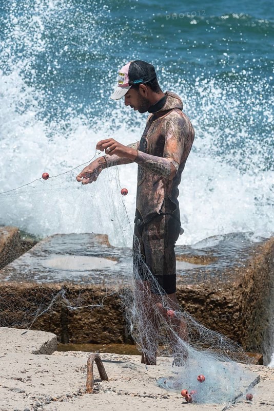 Alexandria, Egypt. June 26th 2024. A young Egyptian fisherman wearing a wetsuit arranges his net on the Mediterranean Sea front of Alexandria, second largest city in Egypt