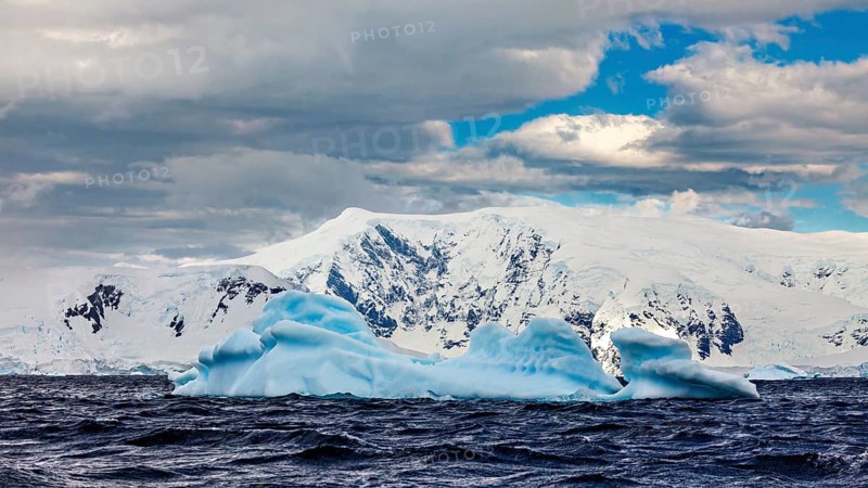 Icebergs floating in undulating water against a backdrop of snow-capped mountains under a dramatic sky, icebergs in the landscape of the Southern Ocean in Antarctica