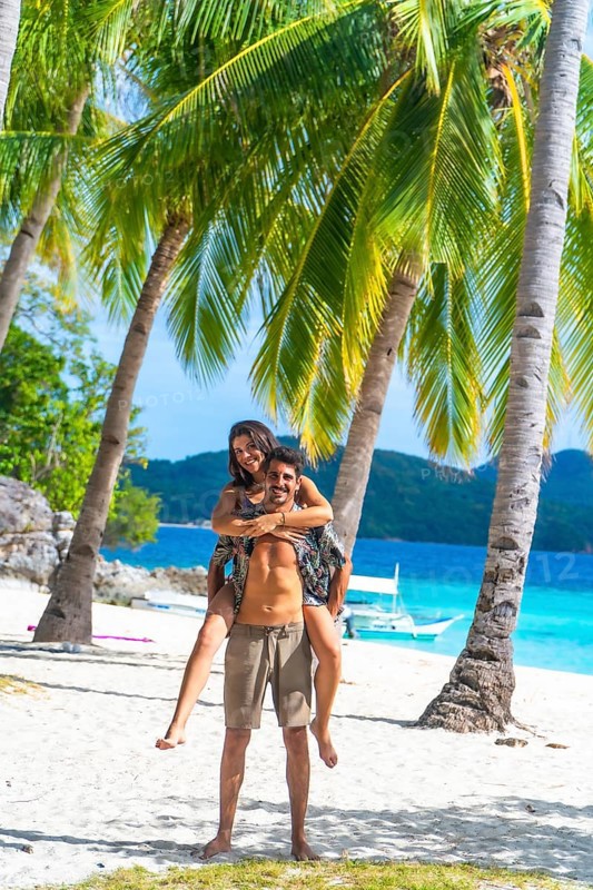Tourists having fun on a beautiful white sand beach with turquoise water and palm trees on malcapuya island, coron, philippines