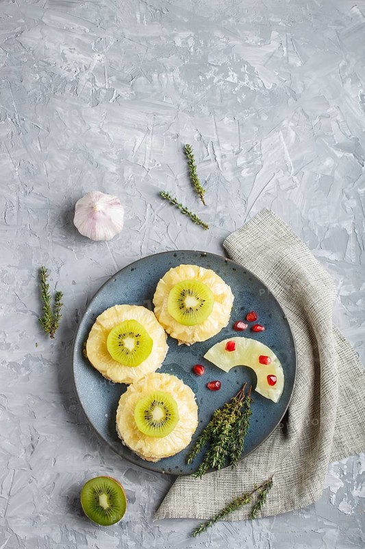 Pieces of baked pork with pineapple, cheese and kiwi on gray background, top view, copy space