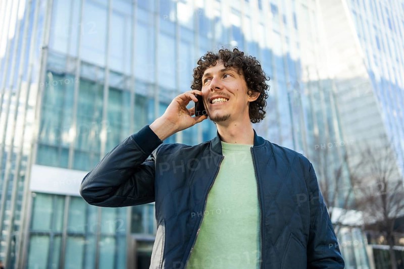 A businessman holds a phone to his ear while walking outside a modern glass building. The image captures a moment of connection and communication in a professional setting