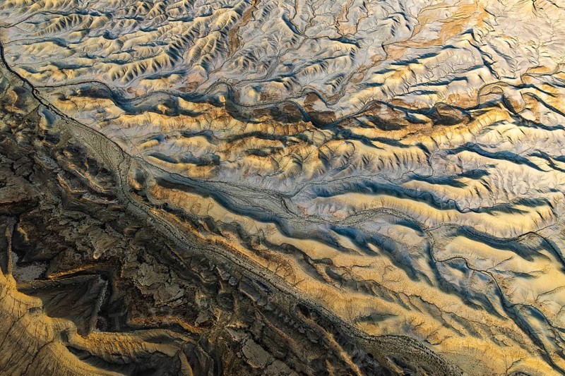 Aerial view showcasing the unique textures of a golden sandstone desert in Utah, USA. The sunlight casts dynamic shadows, highlighting the intricate landscape patterns