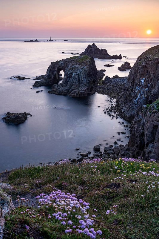 Coastal landscape at Land's End. The rock Enys Dodnan Arch with rock gate. In the foreground, flowering sea carnations (Armeria maritima) . In the evening at sunset. Long exposure. Land's End, Penzance, Cornwall, England, Great Britain