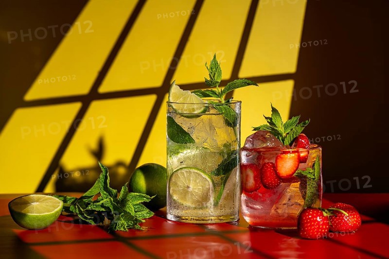 Glasses of classic mojito with lime and mint, and strawberry mojito featuring fresh strawberries, set on a red surface with a warm yellow background, sunlight casting shadows