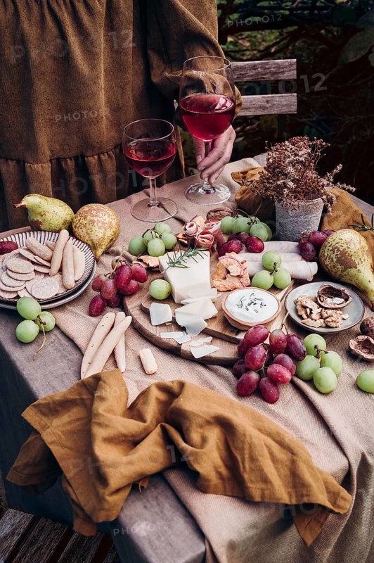 A rustic setup featuring a delicious cheese and fruit platter paired with two glasses of red wine. Grapes, pears, and a variety of cheeses create a perfect snack atmosphere