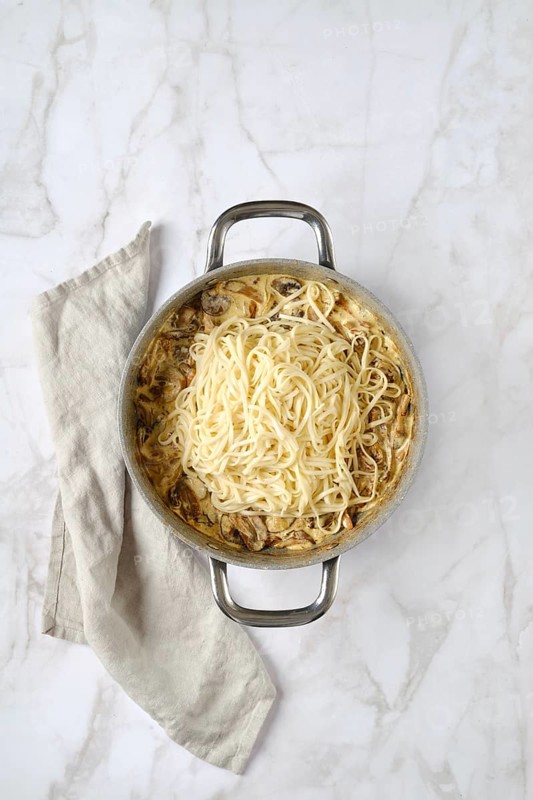 Overhead view of casserole with noodles and chopped champignon, chanterelles, oyster mushrooms and onion