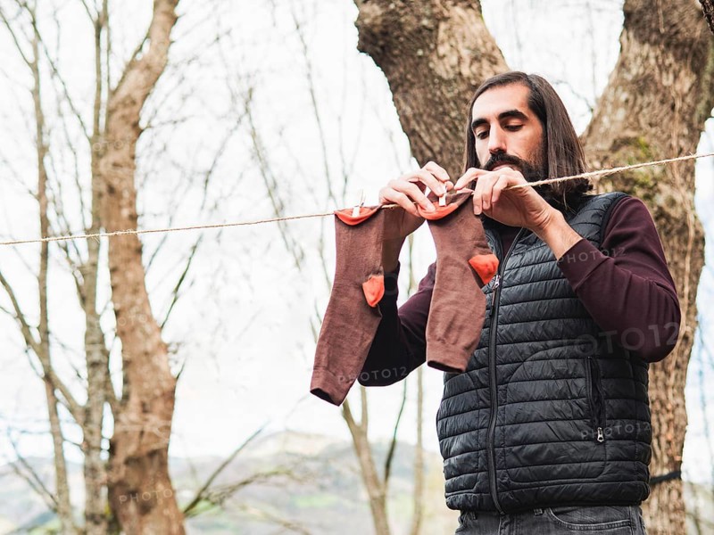 A man hangs clothes on a line in a forest, emphasizing simplicity and nature. The scene highlights harmony with the outdoors, featuring trees and serene surroundings